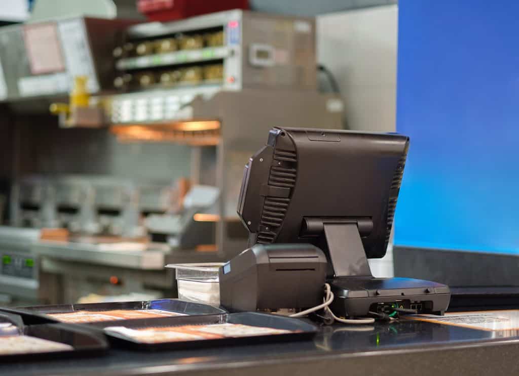 Cash and order desk and kitchen equipment on back in fast food restaurant. POS systems need to be PCI compliant.