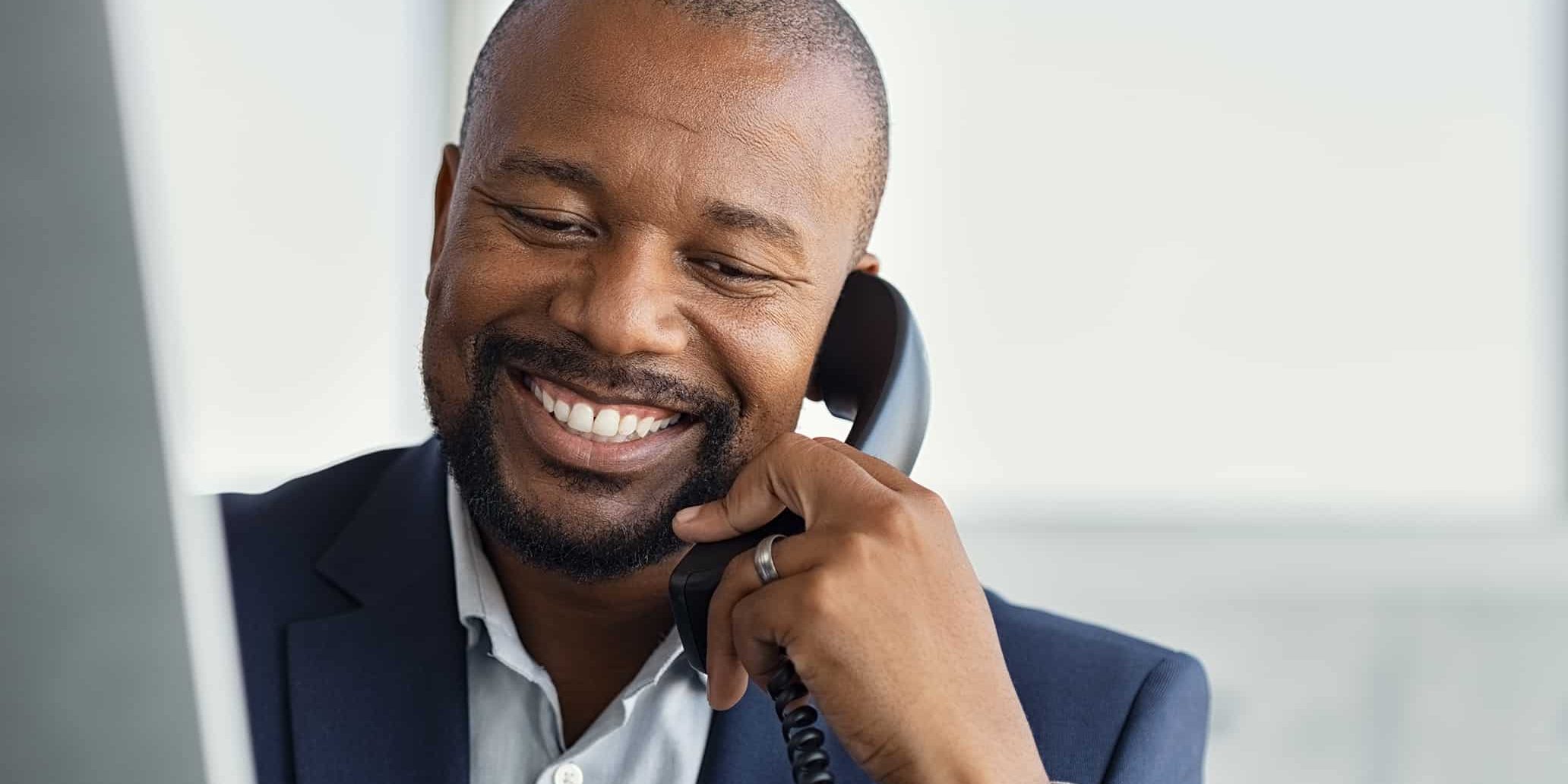 Close up face of mature businessman working on computer and talking on phone. Mature african man talking on mobile phone at desk in office. Smiling manager working at desk with copy space.