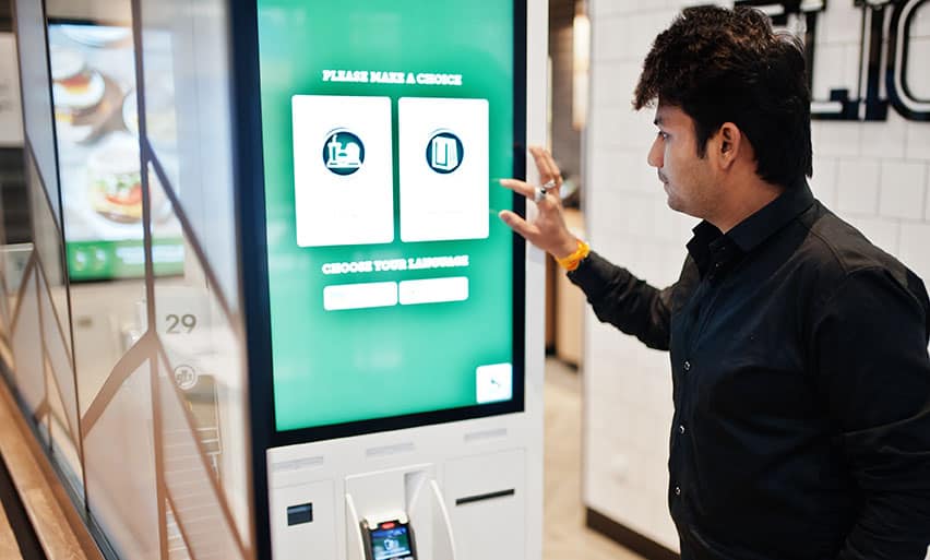 Customer at restaurant places orders and pay through self-pay kiosk for fast food, payment terminal.